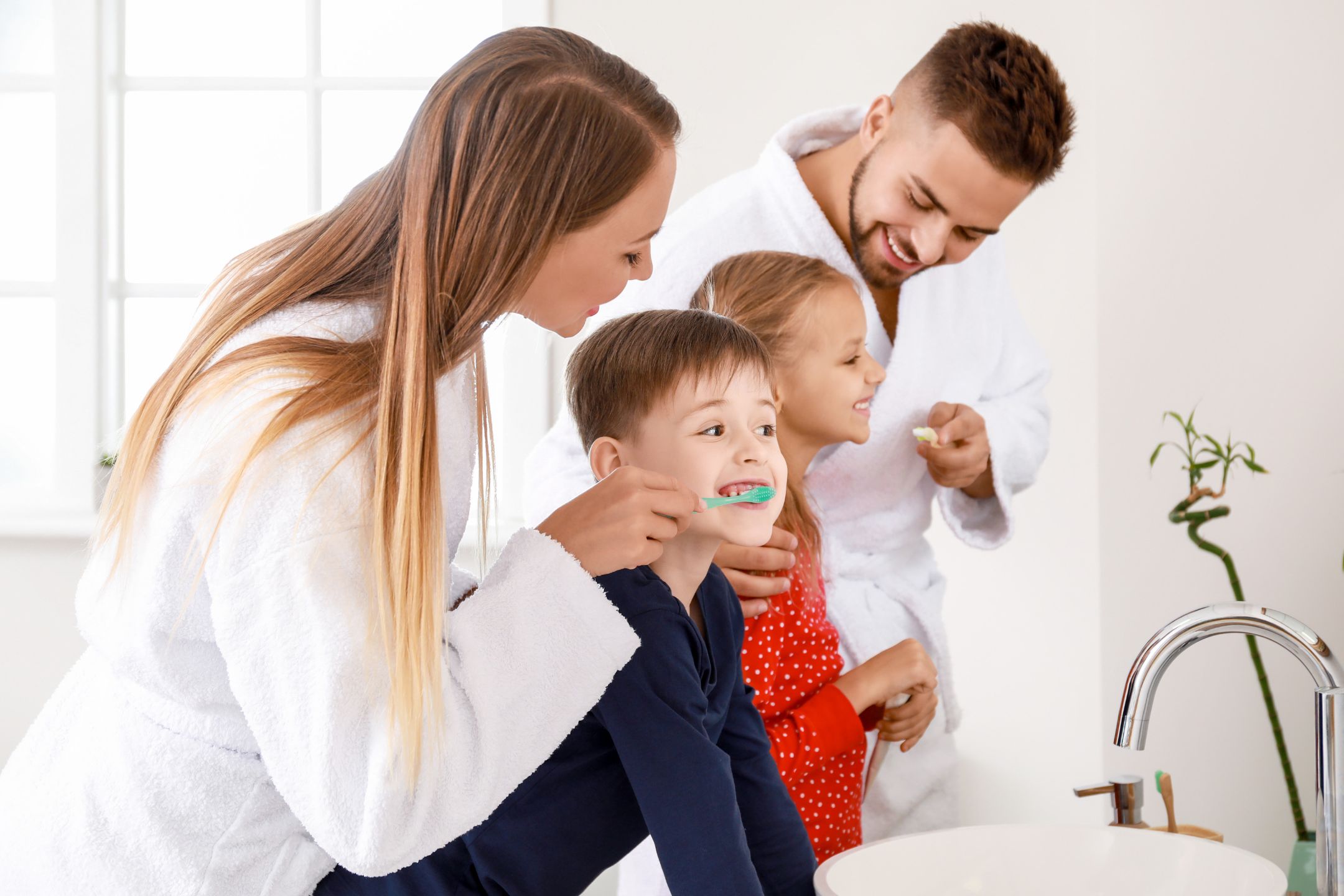 Parents helping their children brush their teeth together in a bright family bathroom.