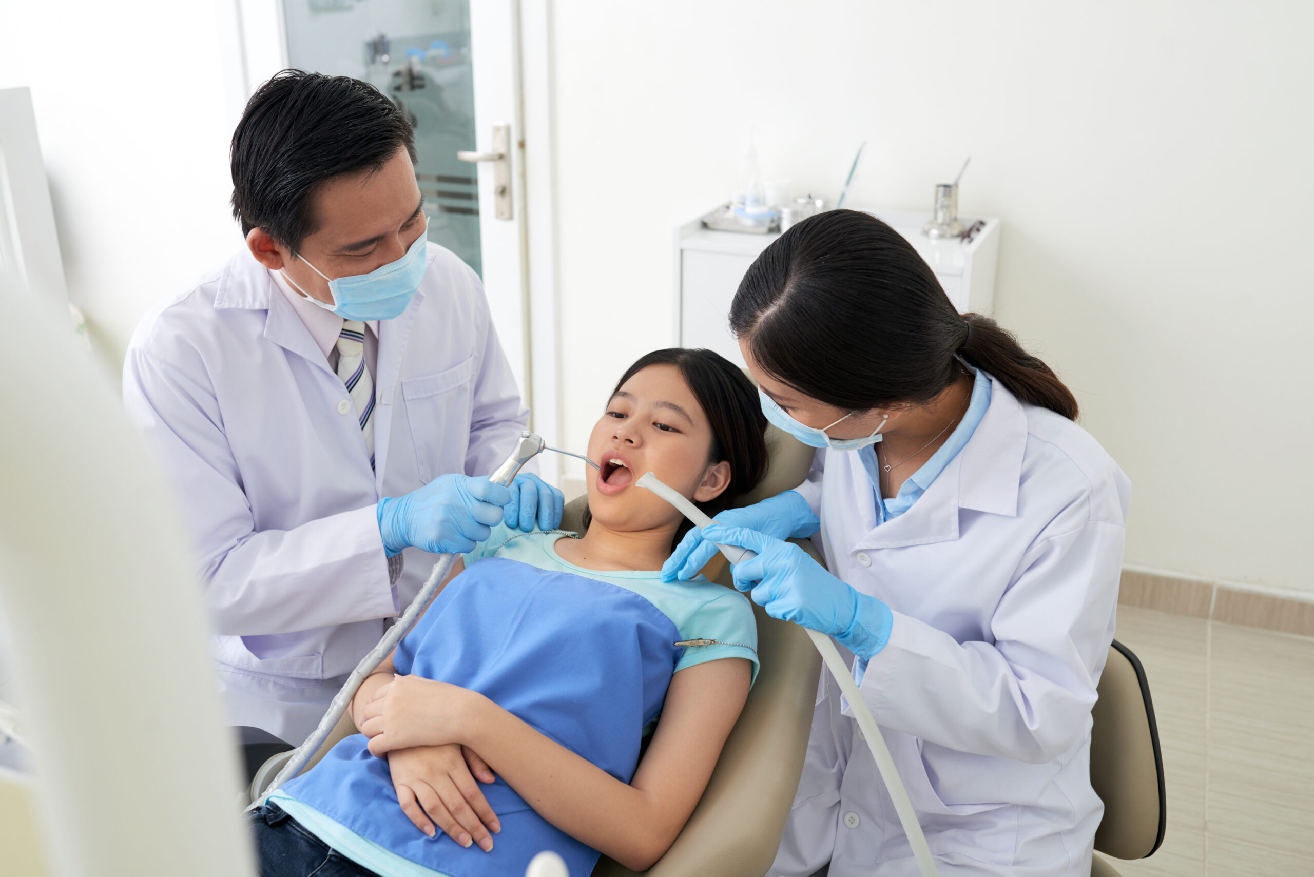 Dentist and assistant performing a dental check-up on a young girl in a modern clinic.
