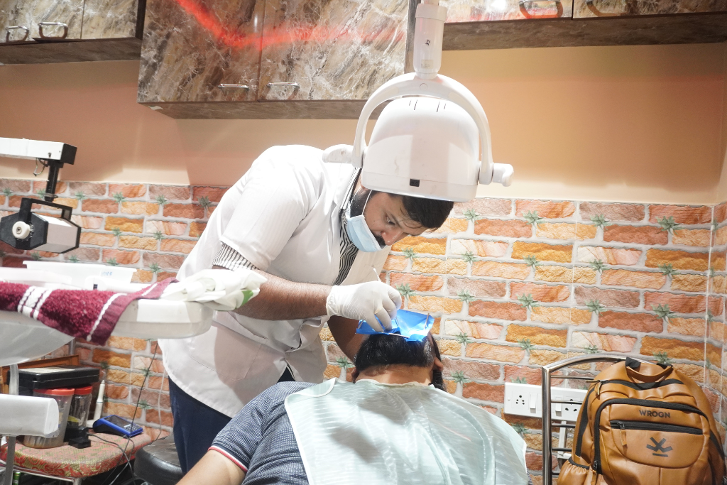 Dentist treating a patient under an overhead light in a clinic, wearing gloves and a mask.
